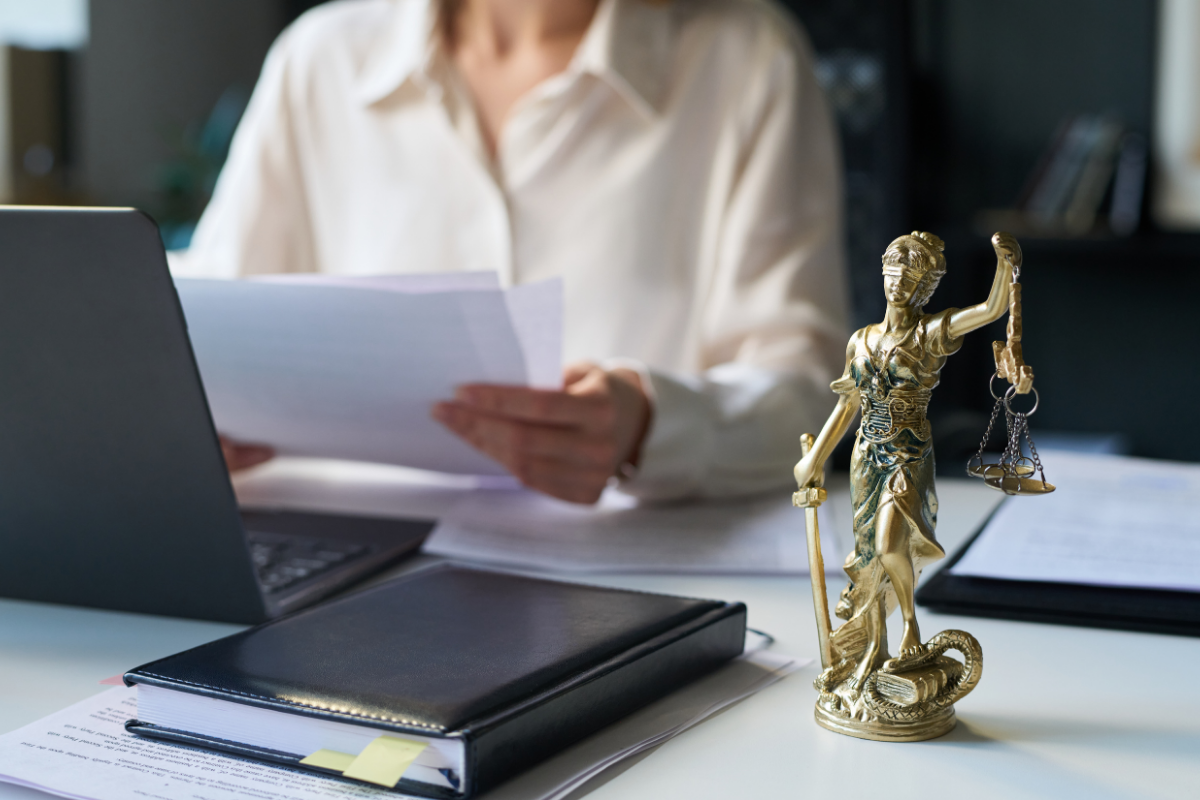 A lawyer working at a desk with a laptop, documents, and a gold Lady Justice statue.