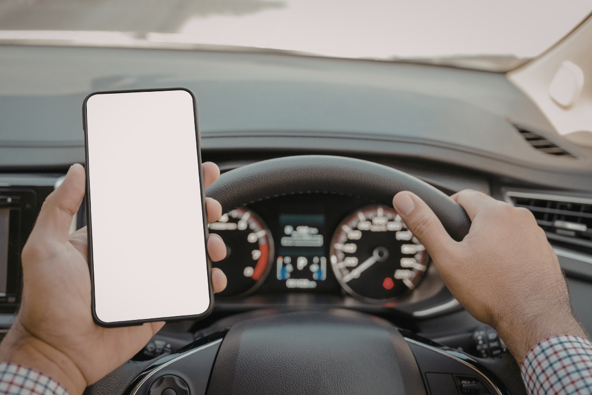 Driver holding a smartphone with a blank white screen while driving a car.