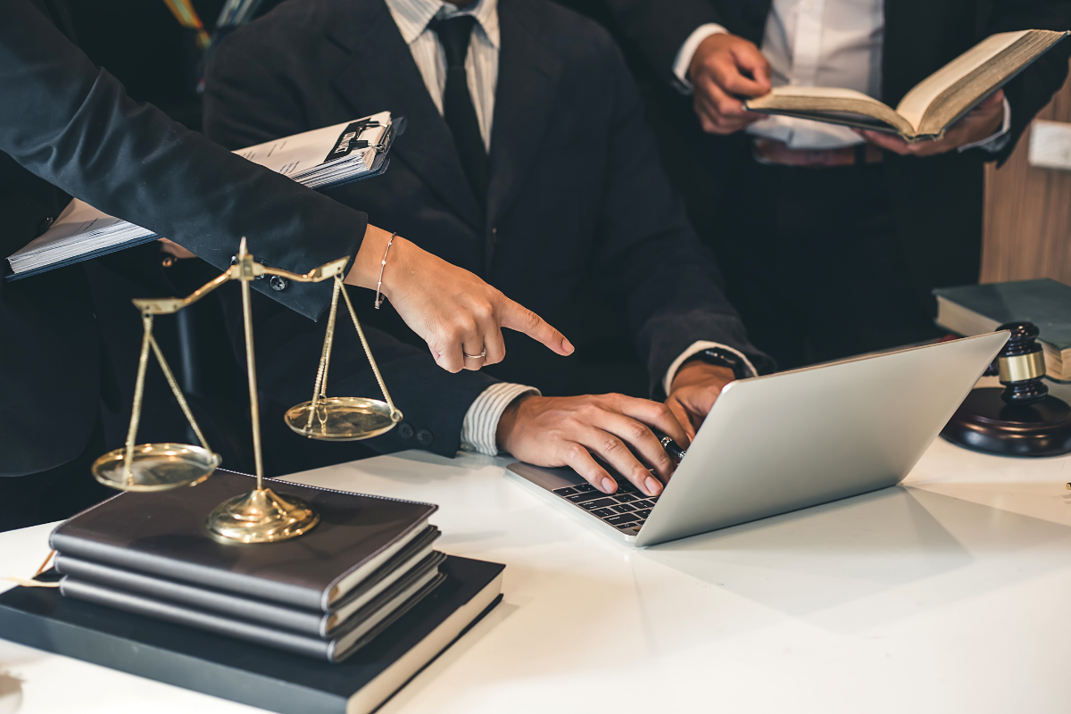 Lawyers collaborating on a legal case with a laptop, law books, scales of justice, and a gavel on a desk.