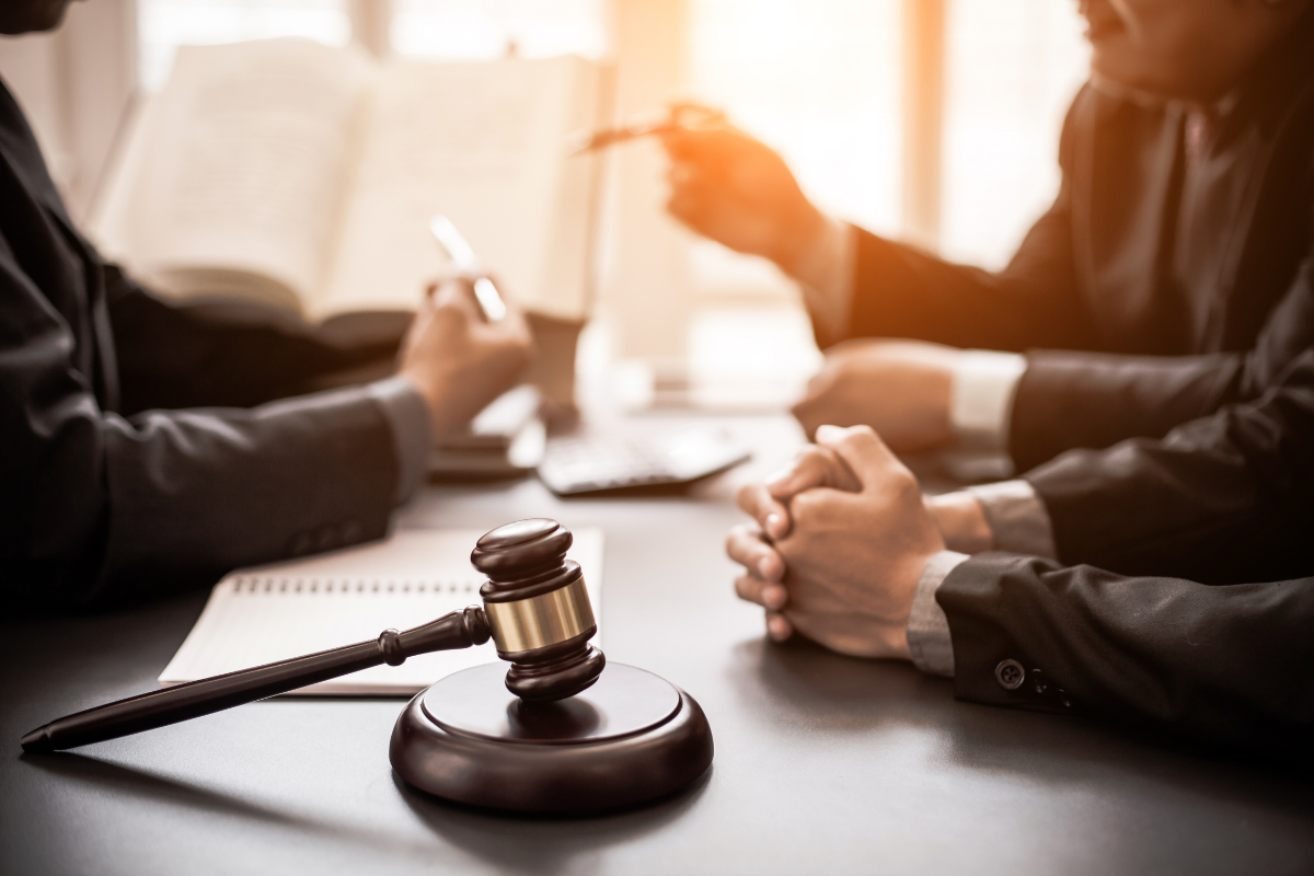 A wooden judge's gavel on a desk with lawyers discussing a legal case in the background.