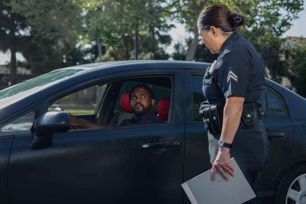 A police officer stands outside a car, speaking with the male driver during a traffic stop.