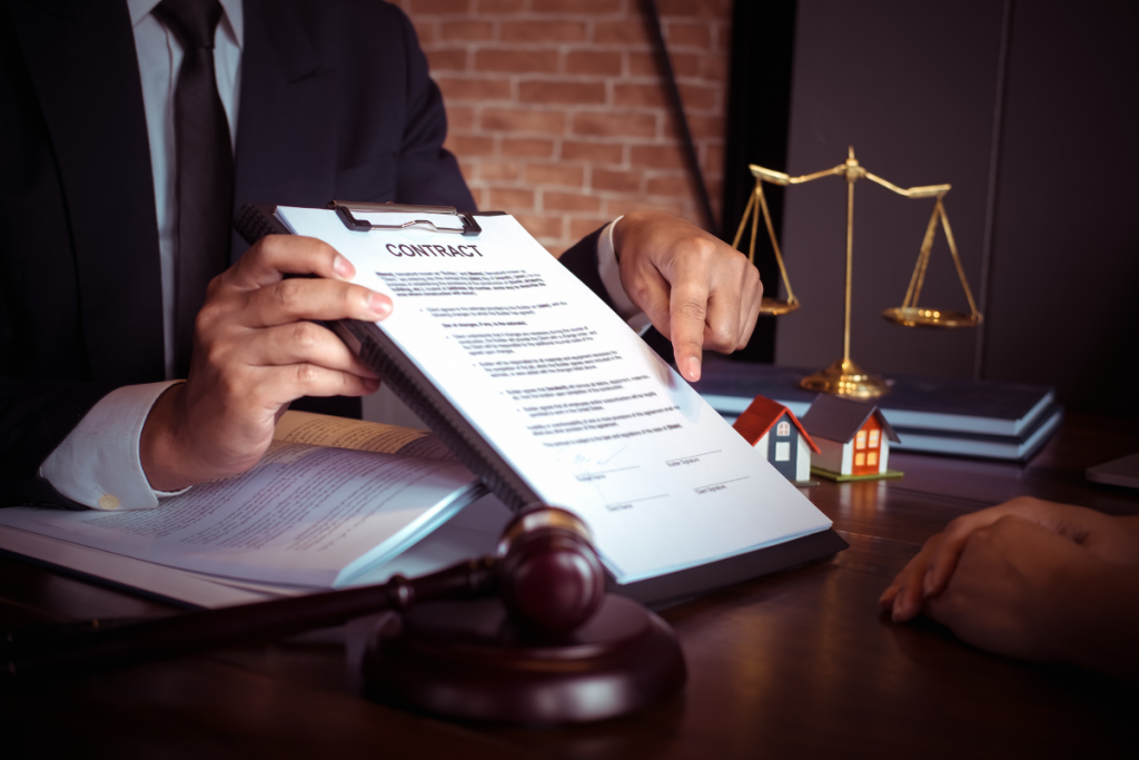 A lawyer in a suit pointing to a contract on a clipboard with a gavel and scales of justice on a desk.
